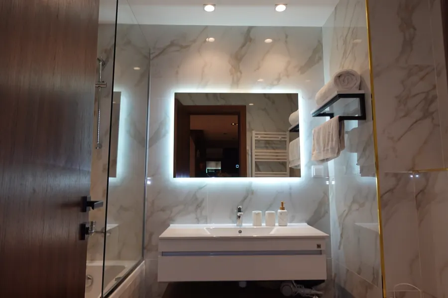 Marble bathroom with backlit mirror and towel shelf