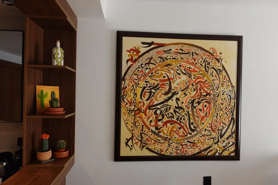 Framed Arabic calligraphy painting beside wooden display shelves