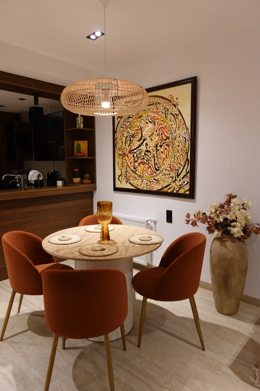 Round dining table with four velvet chairs under a rattan pendant
