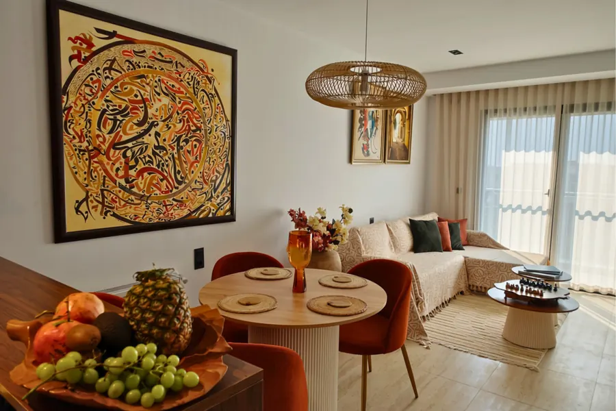 Dining table with a fruit platter, a large Arabic calligraphy painting and the sofa behind