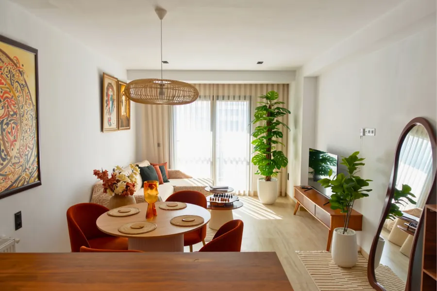 Bright open-plan living room with round dining table, TV and arched mirror